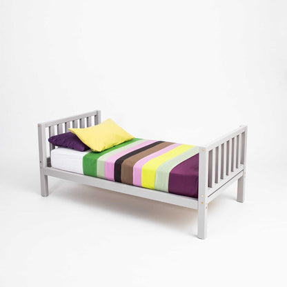 A Sweet Home From Wood raised kids' bed on legs with a headboard and footboard, made of solid wood, promoting independence and adorned with colorful striped sheets.