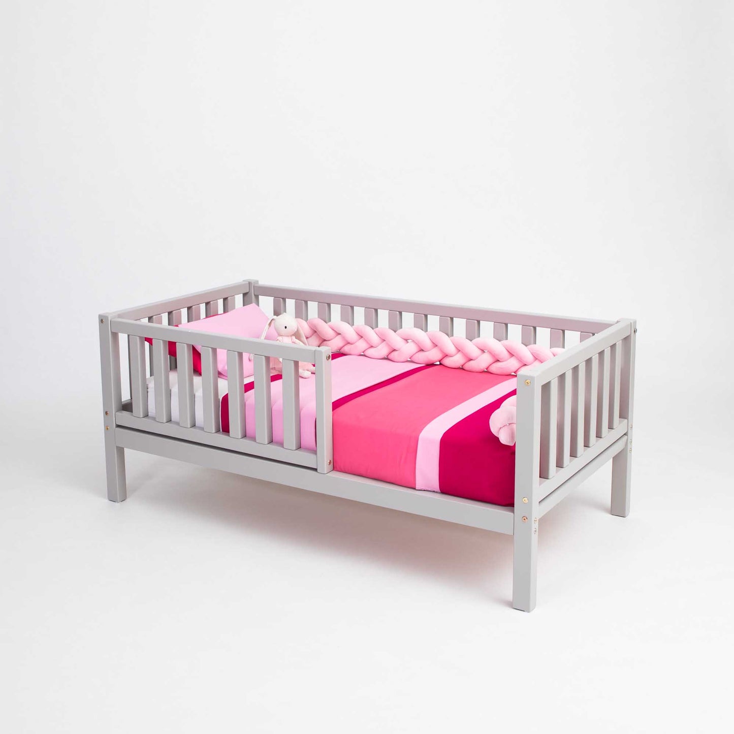 A Sweet Home From Wood toddler bed on legs with a fence and a pink and grey blanket for independent sleeping.