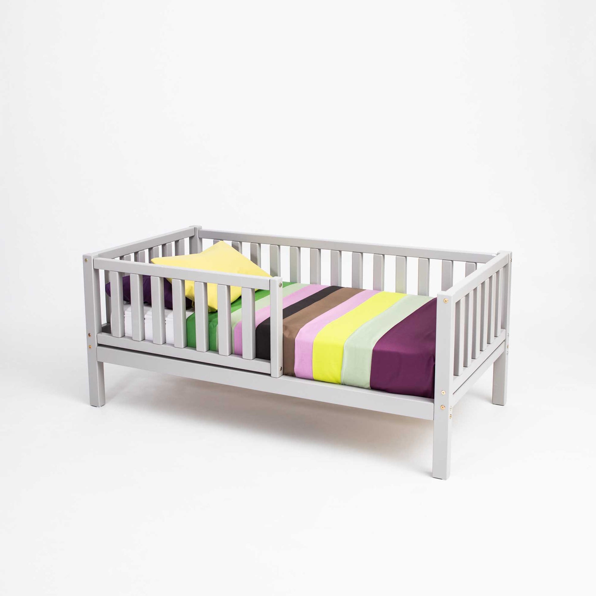 A Sweet Home From Wood toddler bed on legs with a fence, with a colorful striped sheet, perfect for independent sleeping.