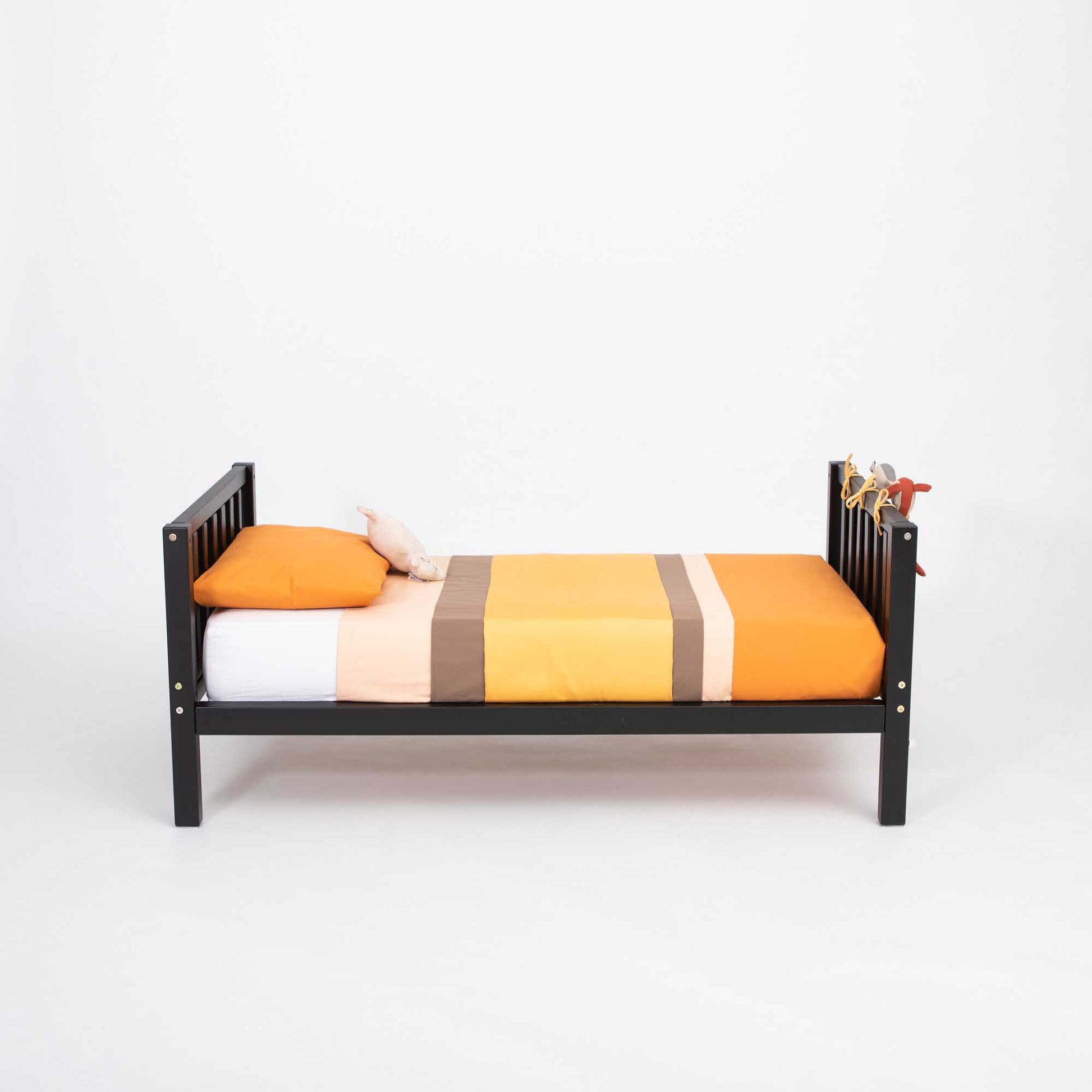 A Sweet Home From Wood Raised kids' bed on legs with a headboard and footboard, made of solid wood and inspired by Montessori, providing independence and adorned with an orange and yellow comforter.