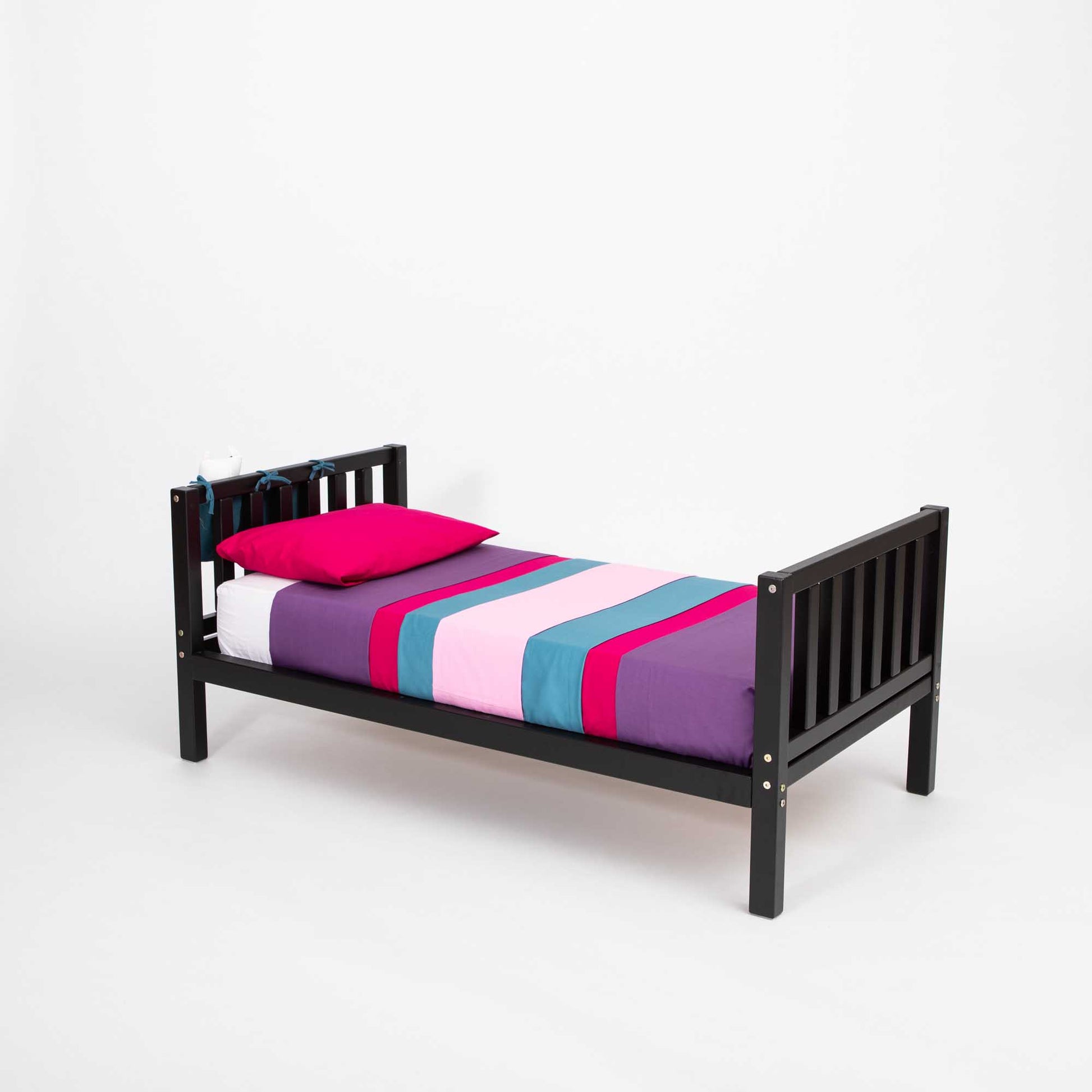 A 2-in-1 kid's bed on legs with a vertical rail headboard and footboard with a black frame and a pink and purple striped sheet.