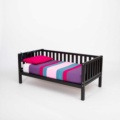 A Sweet Home From Wood 2-in-1 toddler bed on legs with a 3-sided vertical rail with a pink and purple striped sheet.