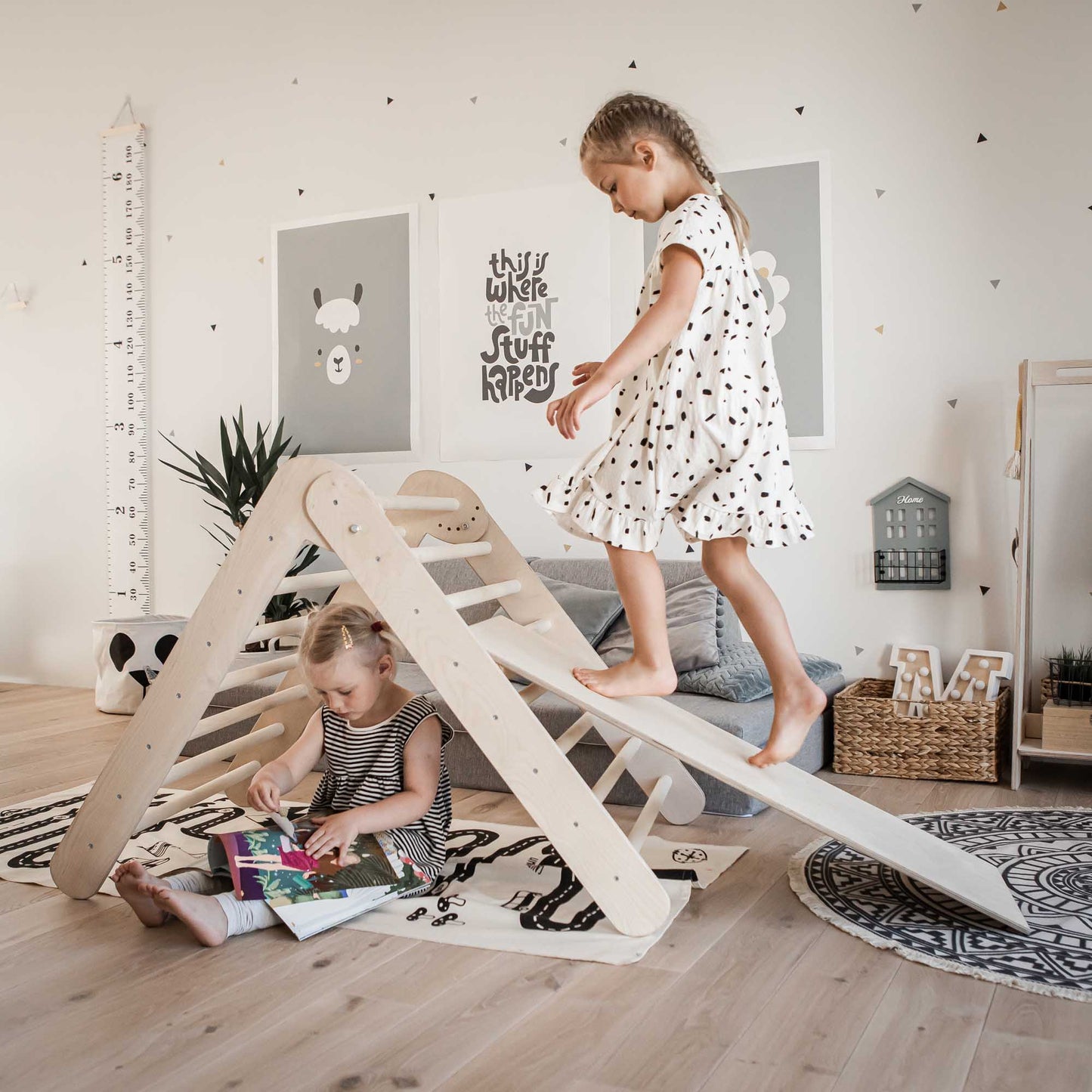 Two girls playing with a Foldable climbing triangle with 2 slope levels in a living room, enhancing their motor skills.