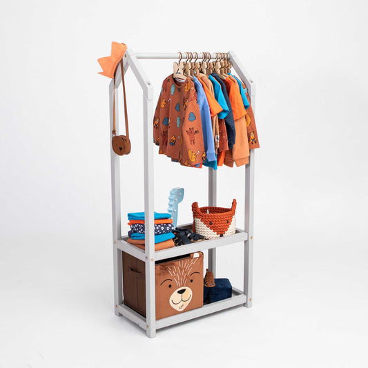 An open Montessori wardrobe with toddler clothing hanging on a Sweet Home From Wood clothing rack.