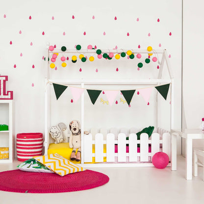 A children's room with a platform house bed with a picket fence and pink and white decorations.