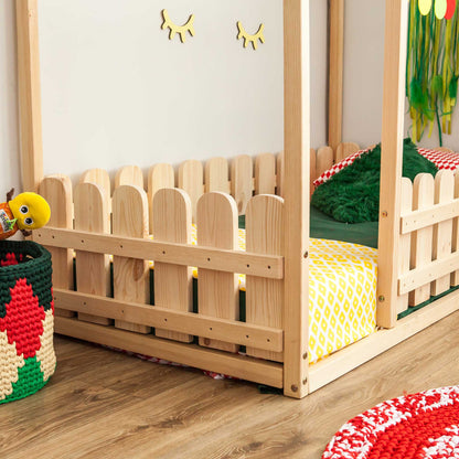 A platform house bed with a picket fence made of wood in a child's room.