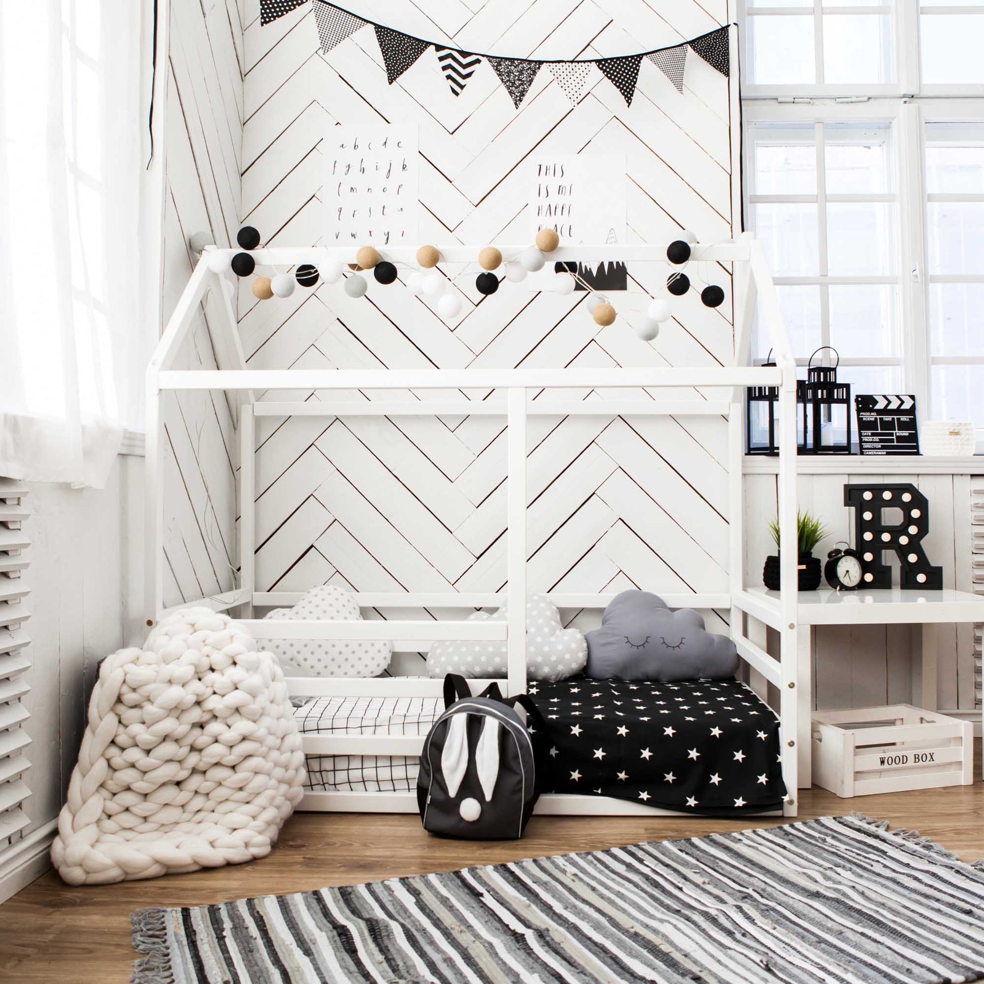 A floor level house bed with a horizontal fence in a white and black themed kids room, complete with a rug.