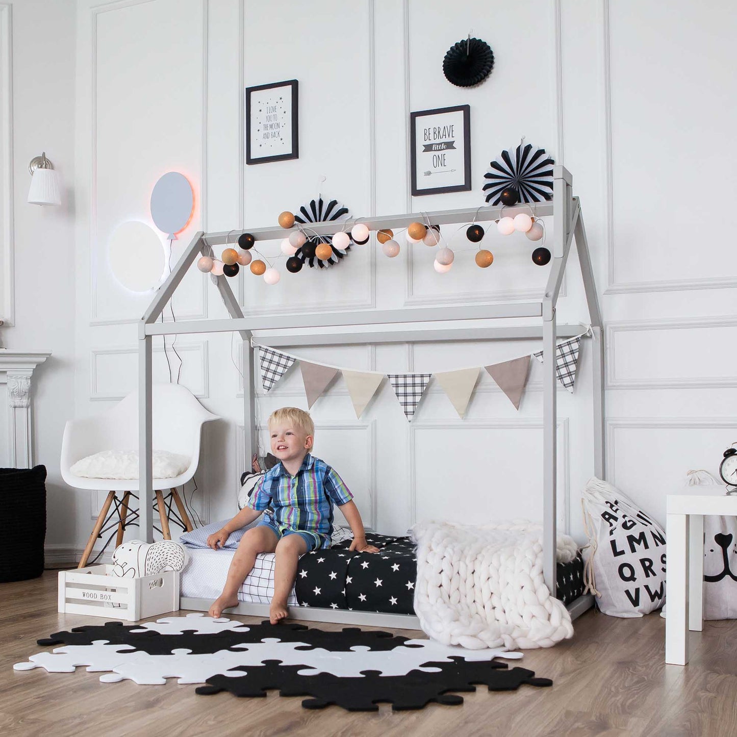 A child is sitting on a Sweet Home From Wood Wooden zero-clearance house bed in a room with black and white decorations.