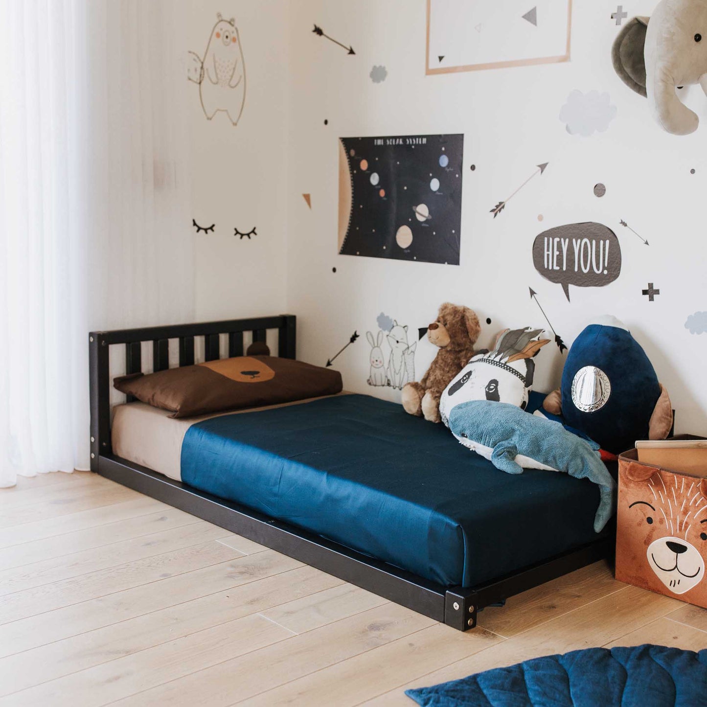 A child's room with a Sweet Home From Wood 2-in-1 toddler bed on legs with a vertical rail headboard and stuffed animals.