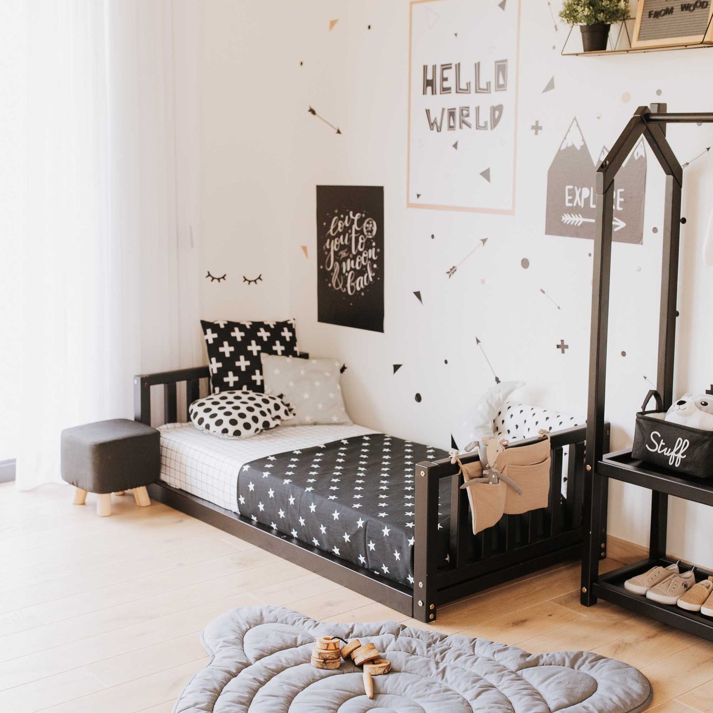 A child's room with a 2-in-1 kid's bed on legs with a vertical rail headboard and footboard made of solid pine or birch wood and black and white decor.