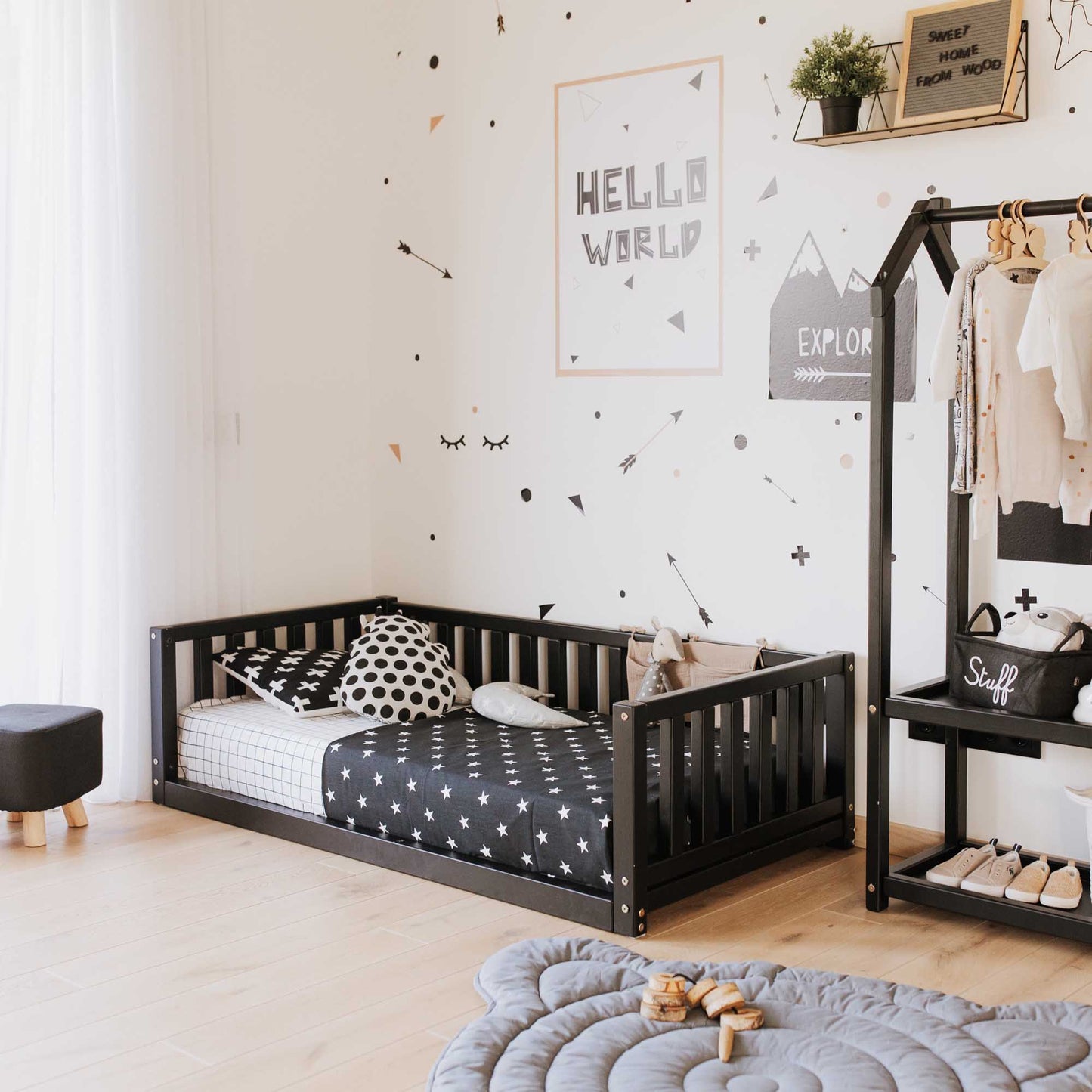 A black and white children's room with a Montessori bed with 3-sided rails from Sweet Home From Wood and shelves.
