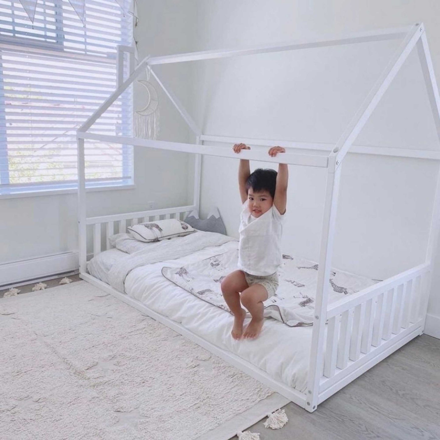 A child is peacefully nestled on top of a Sweet Home From Wood toddler house bed with a headboard and footboard.