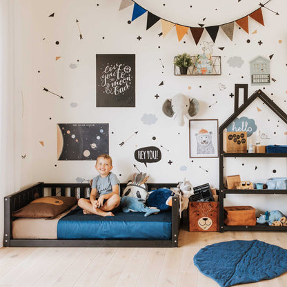 A Montessori-inspired boy's room with a Sweet Home From Wood 2-in-1 toddler bed on legs with a 3-sided vertical rail, shelves, and a star wall.