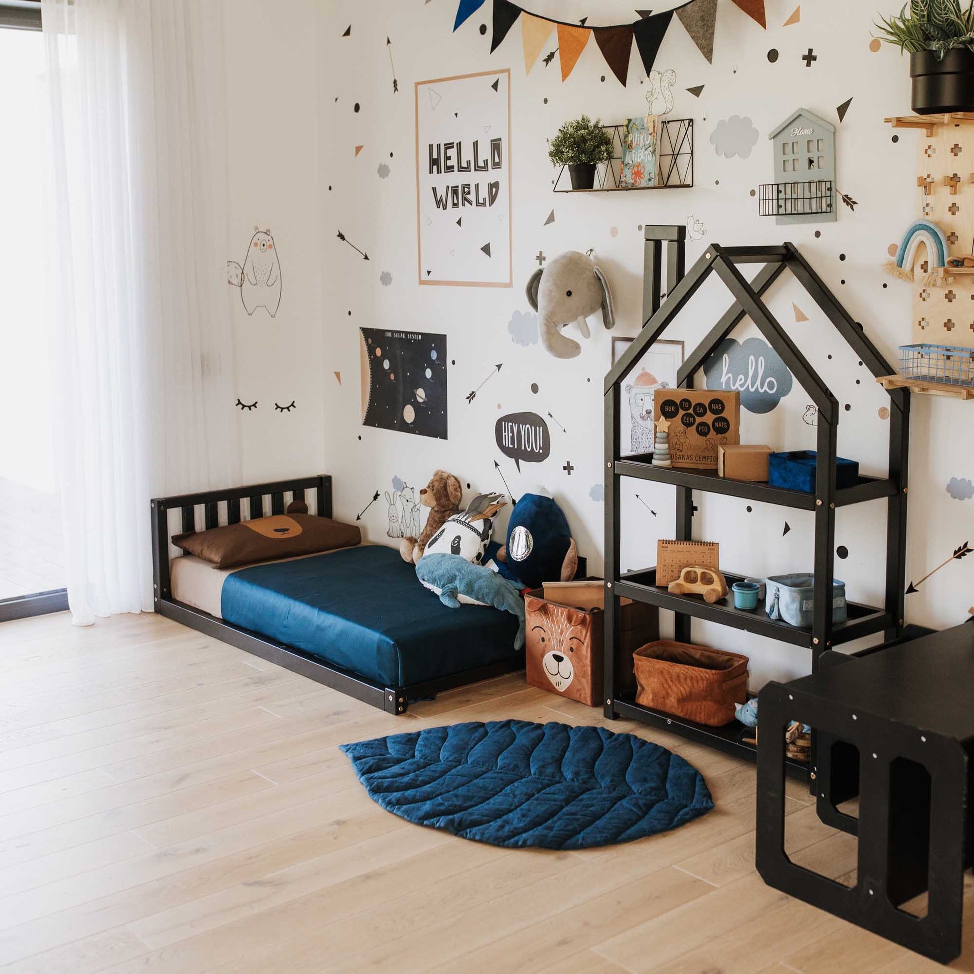 A children's room with a Sweet Home From Wood 2-in-1 toddler bed on legs with a vertical rail headboard, made of solid pine or birch wood, following a black and blue theme.
