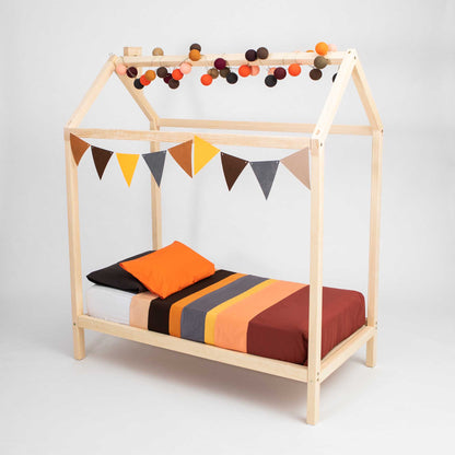 A wooden house bed on legs with bunting and pom poms.