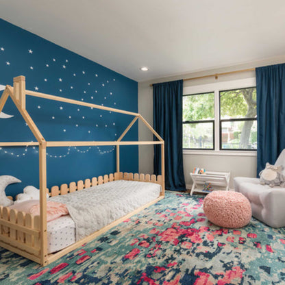 A children's room with blue walls and a Floor house-frame bed with 3-sided picket fence rails.