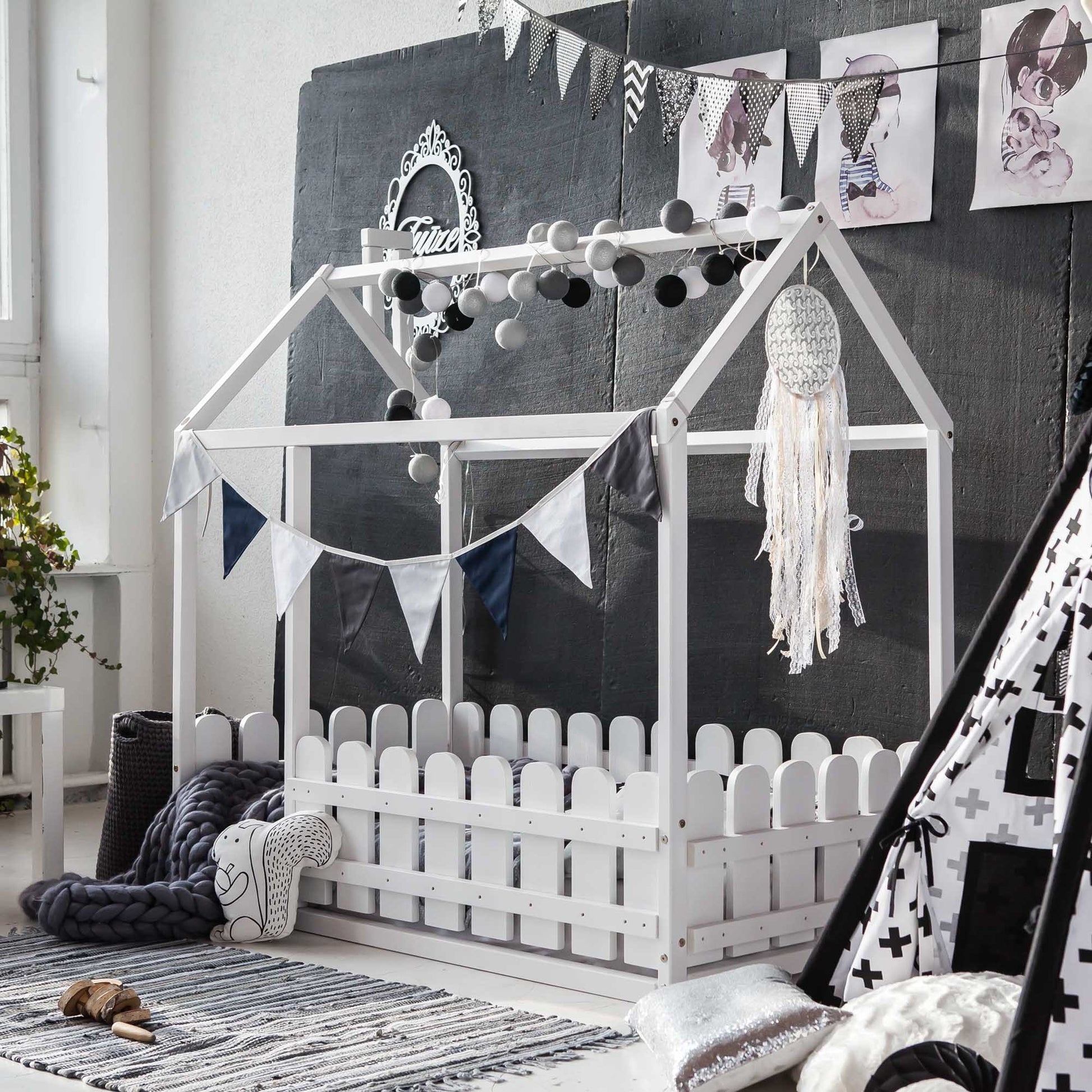A child's room with a teepee bed and a platform house bed with a picket fence.