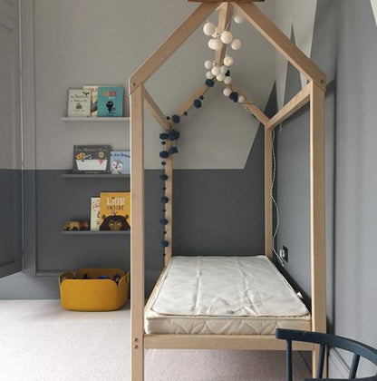 A child's bedroom with a wooden house bed on legs.