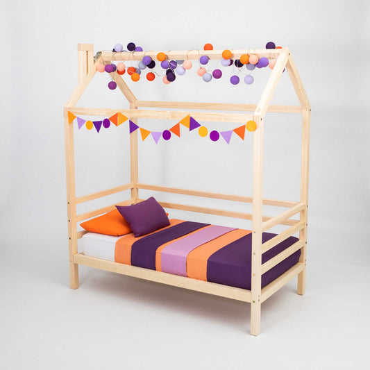 A Children's house bed on legs with 3-sided rails with purple and orange pom poms.