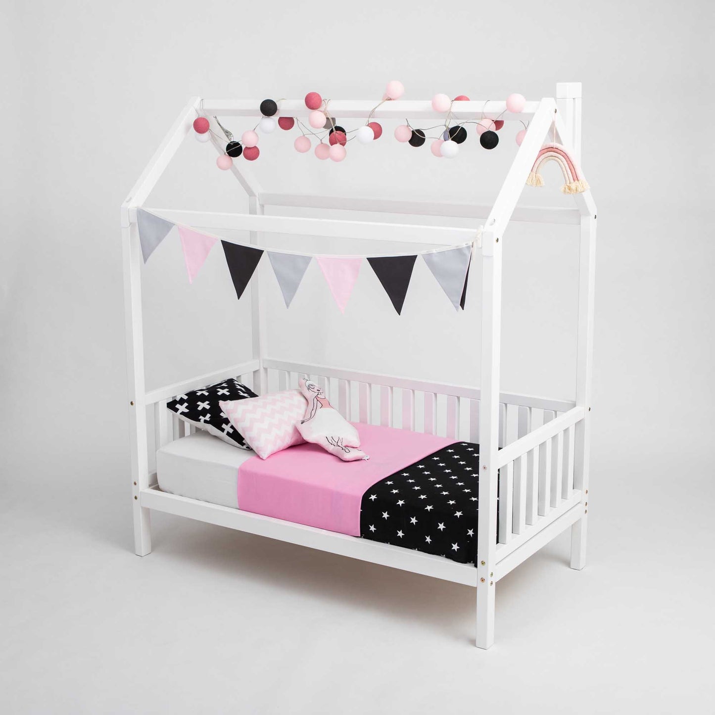 A raised house bed on legs with 3-sided rails, with pink and black polka dot bedding.