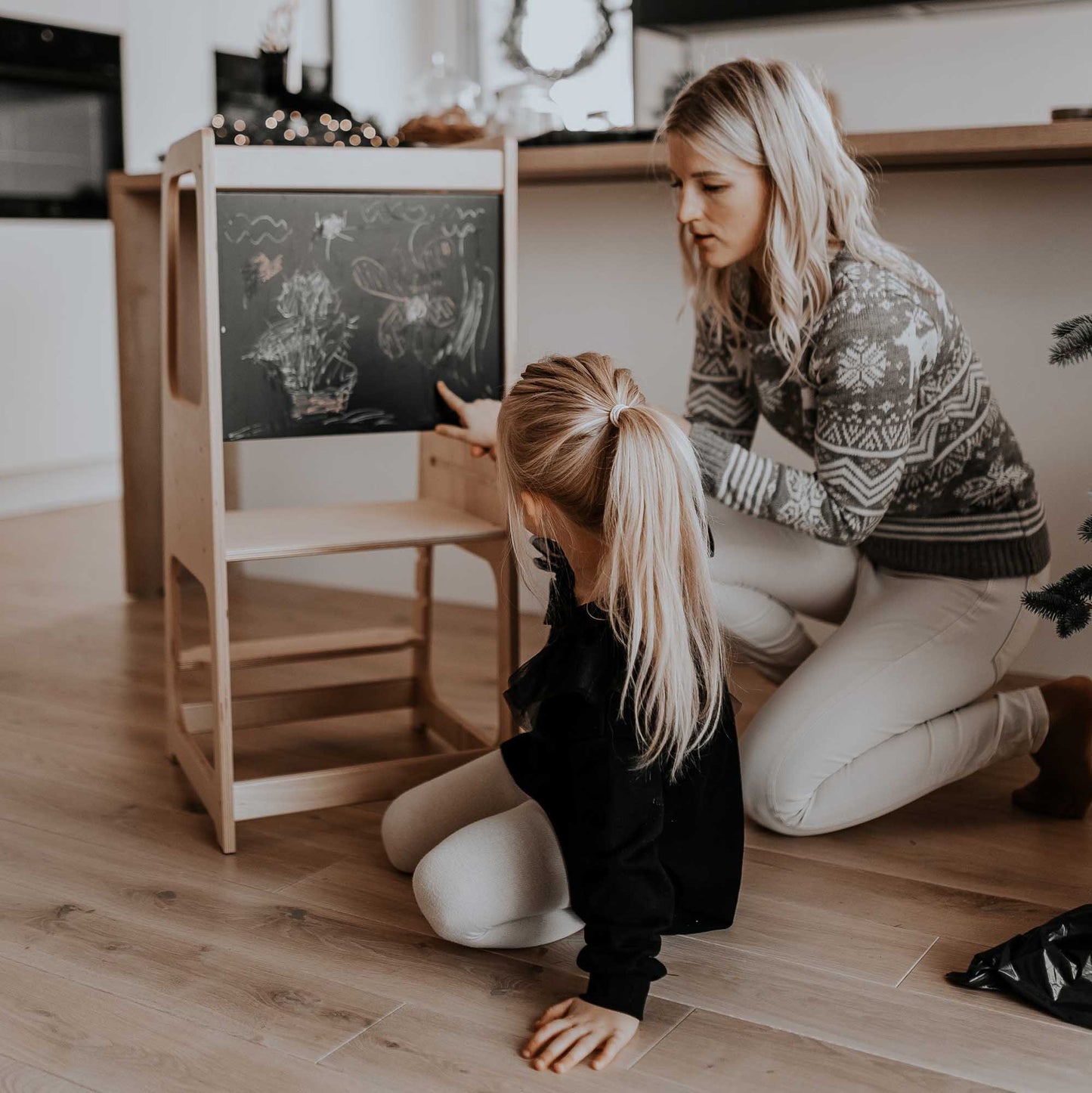 A mother and daughter using a Sweet Home From Wood kitchen tower with blackboard to draw on a wooden easel.