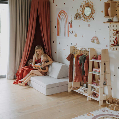 A girl is sitting on a bed in a child's room with an open Sweet Home From Wood children's wardrobe nearby.