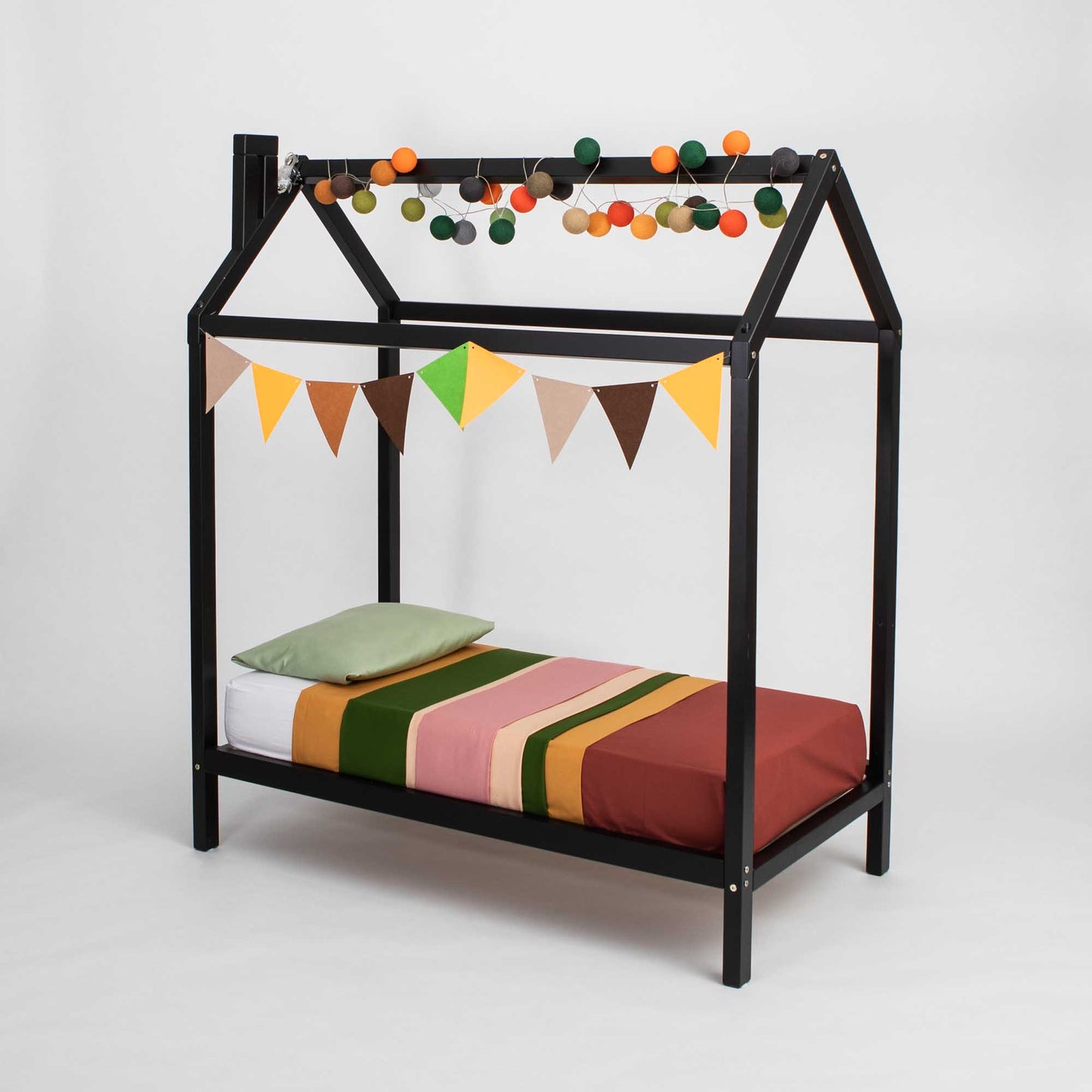 A bed with a black frame and bunting hanging from it, designed as a wooden house bed on legs.