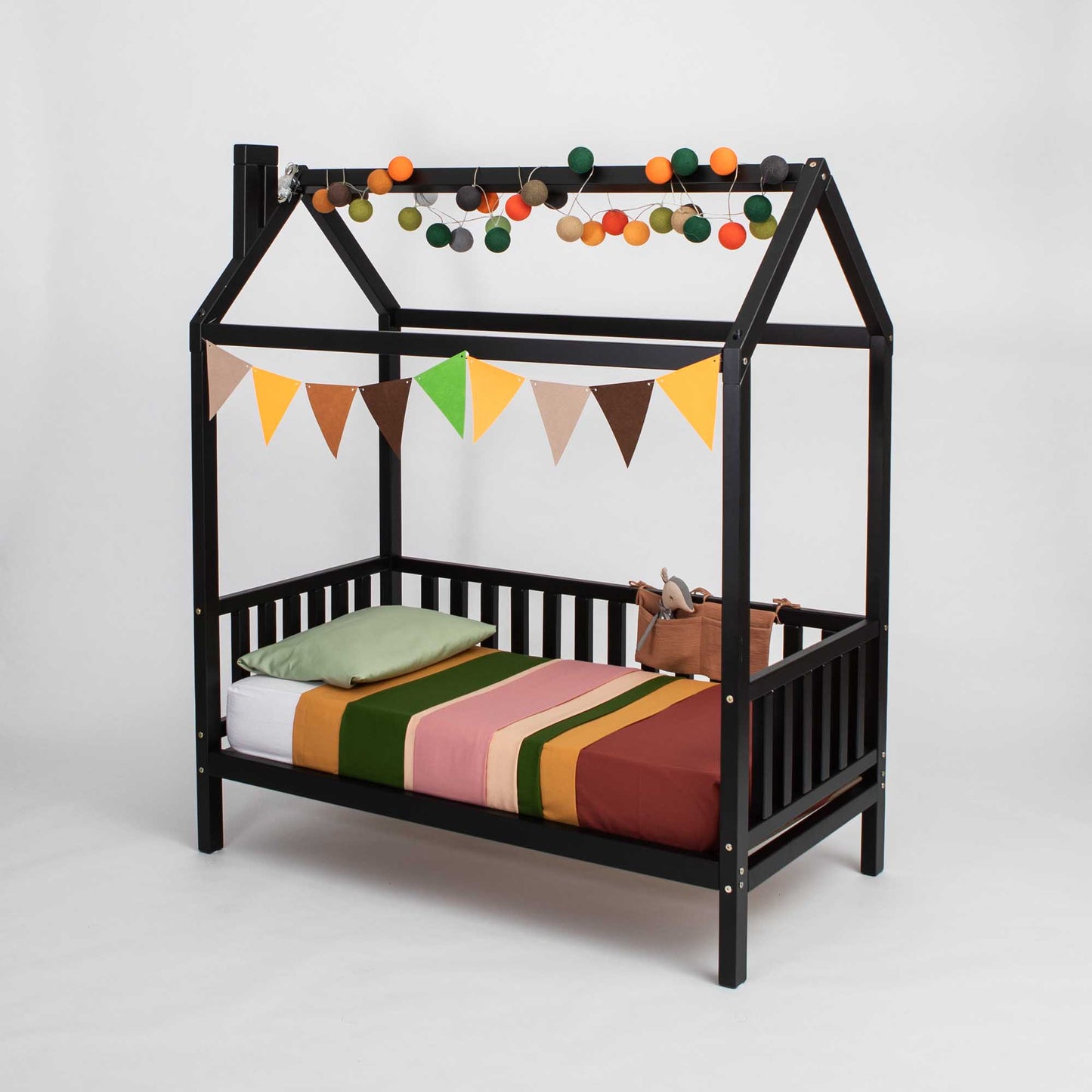 A raised house bed on legs with 3-sided rails for children with a black canopy and bunting.