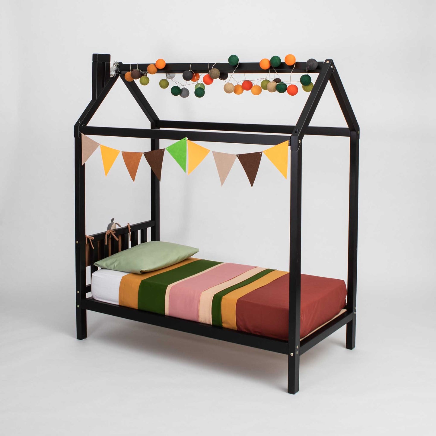 A Toddlers' house bed on legs with a headboard with a bunting hanging from it.