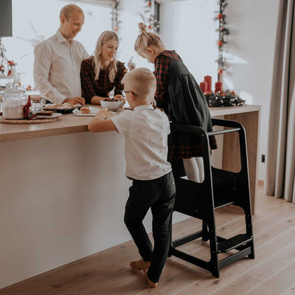 Family of four cooking together, with the daughter actively participating while standing on a toddler step stool. Encouraging inclusive family moments in the kitchen.