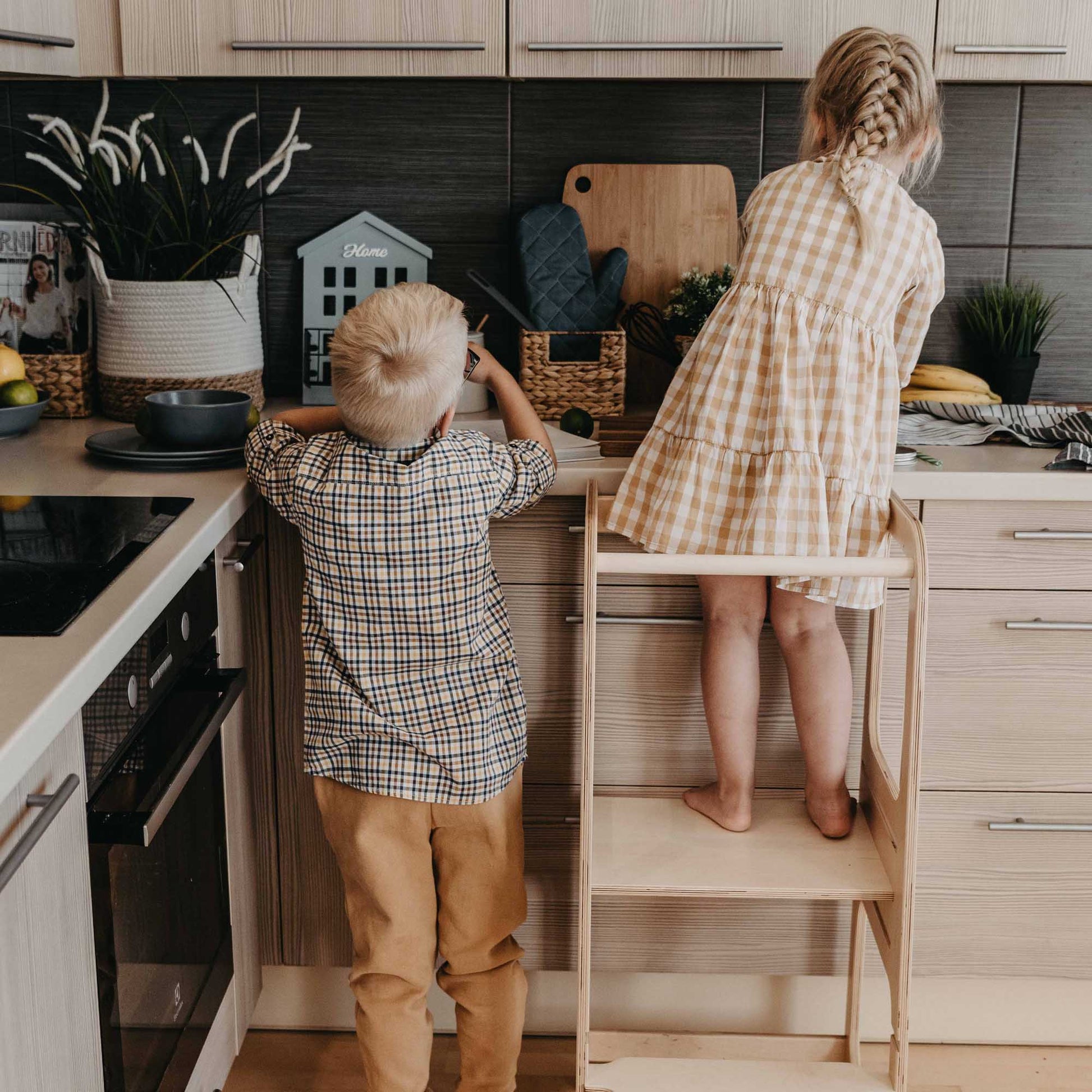 Two children standing on a Sweet Home From Wood Kids' kitchen tower with 3 height levels in a kitchen.