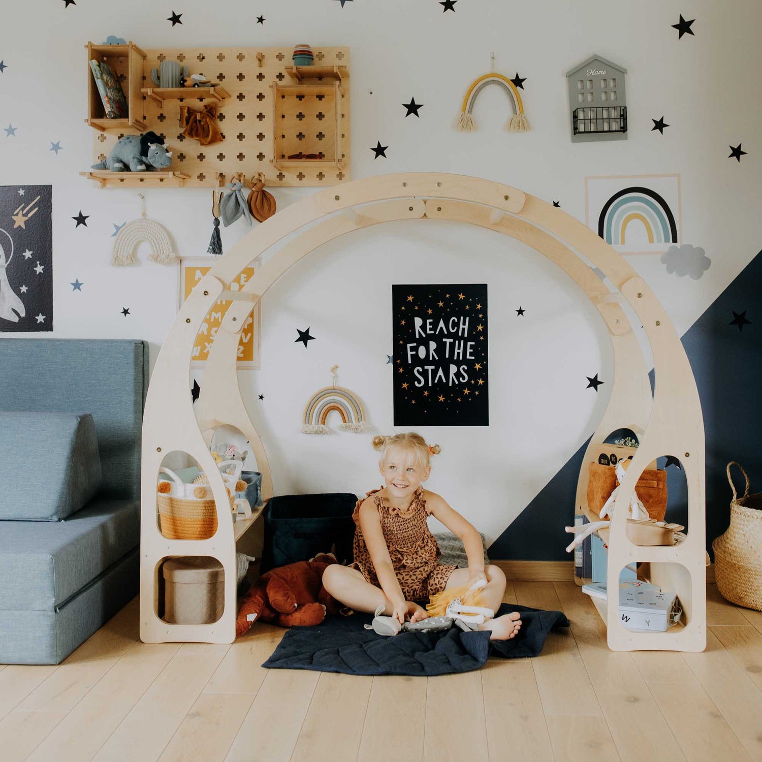 A child's room with a Sweet Home From Wood wooden arch, an open Sweet Home From Wood toy storage shelf, and stars on the wall.