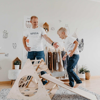 A dad playing with a boy engaged in play on a transformable climbing triangle with three sensory sides, both enjoying a dynamic and stimulating play experience together.