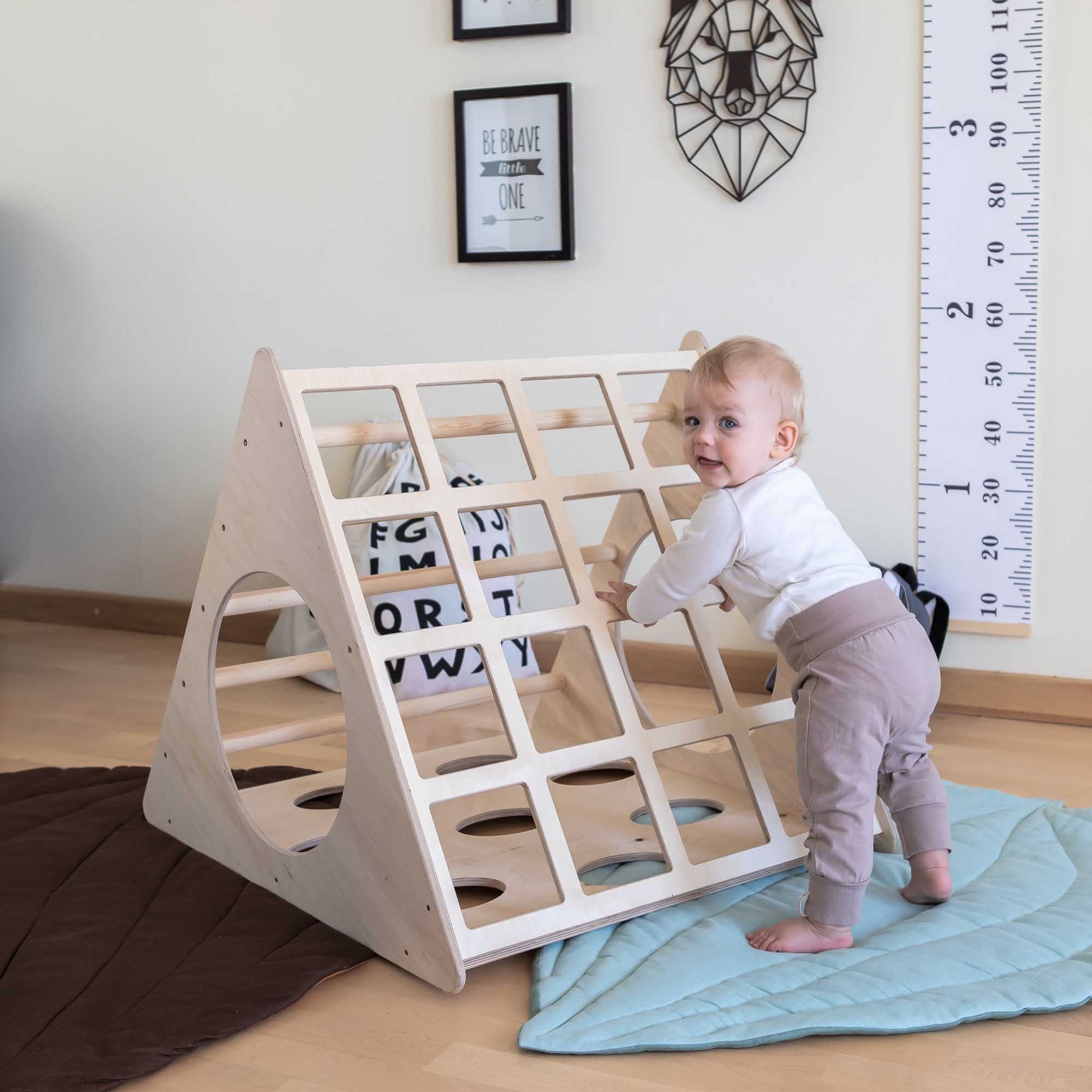 A baby is playing with a climbing triangle with sensory panels indoors.