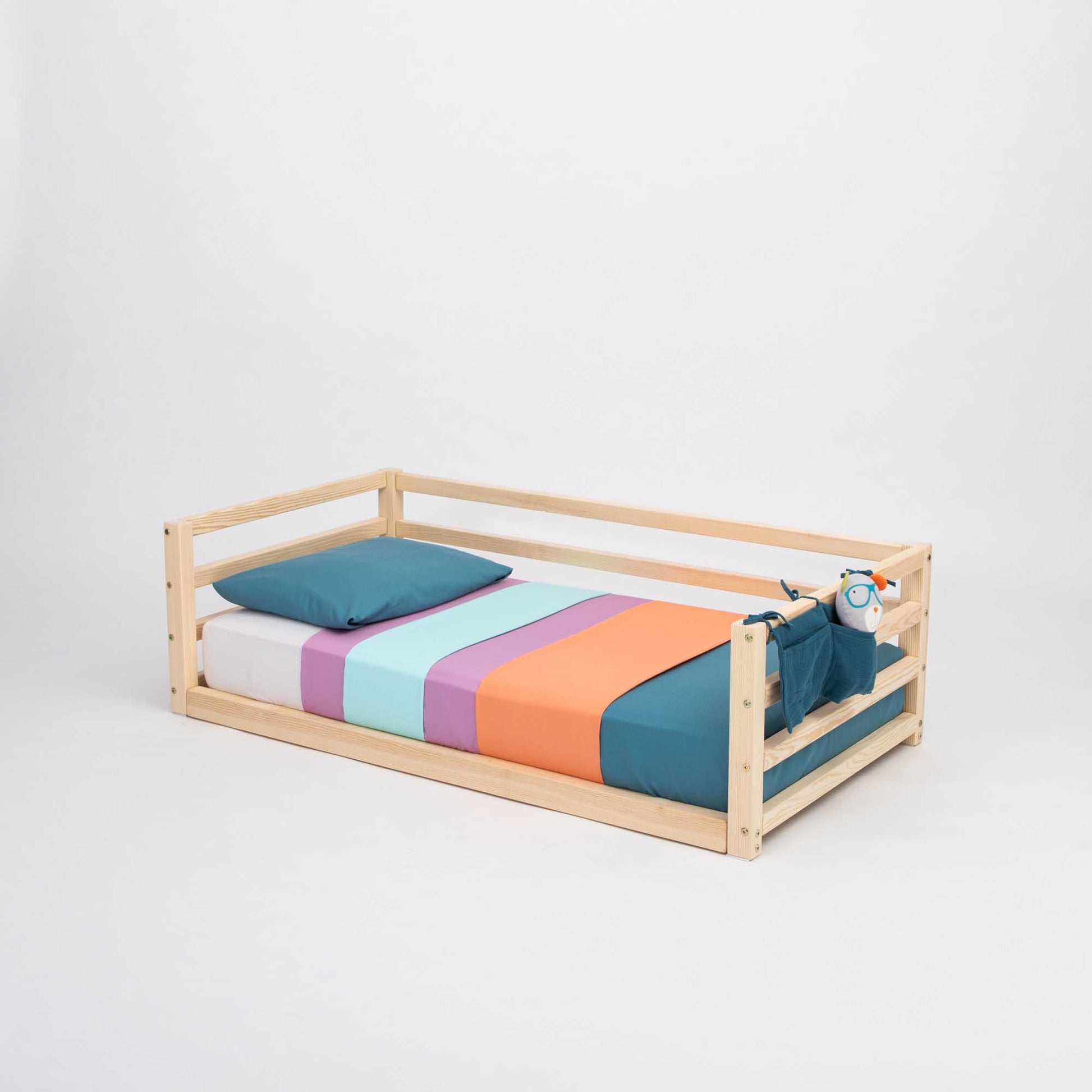 A Sweet Home From Wood transitional children's floor level bed with colorful sheets and a wooden frame.
