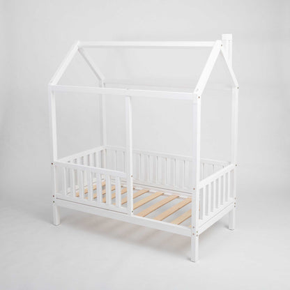 A white kids' house bed on legs with a fence and wooden slats.