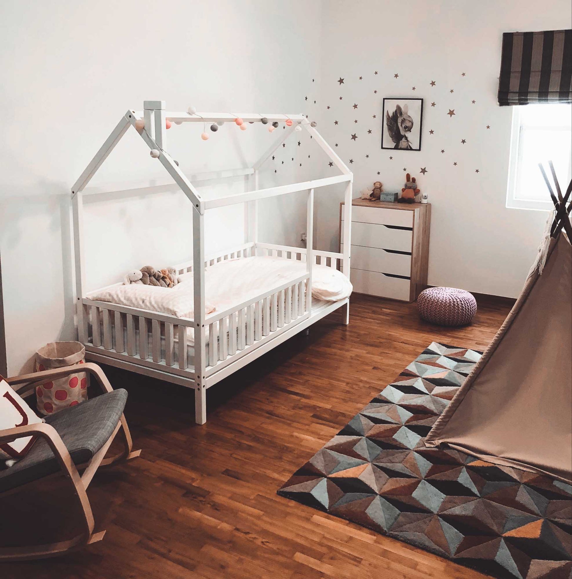 A toddler's room with a kids' house bed on legs with a fence, teepee, and chair.