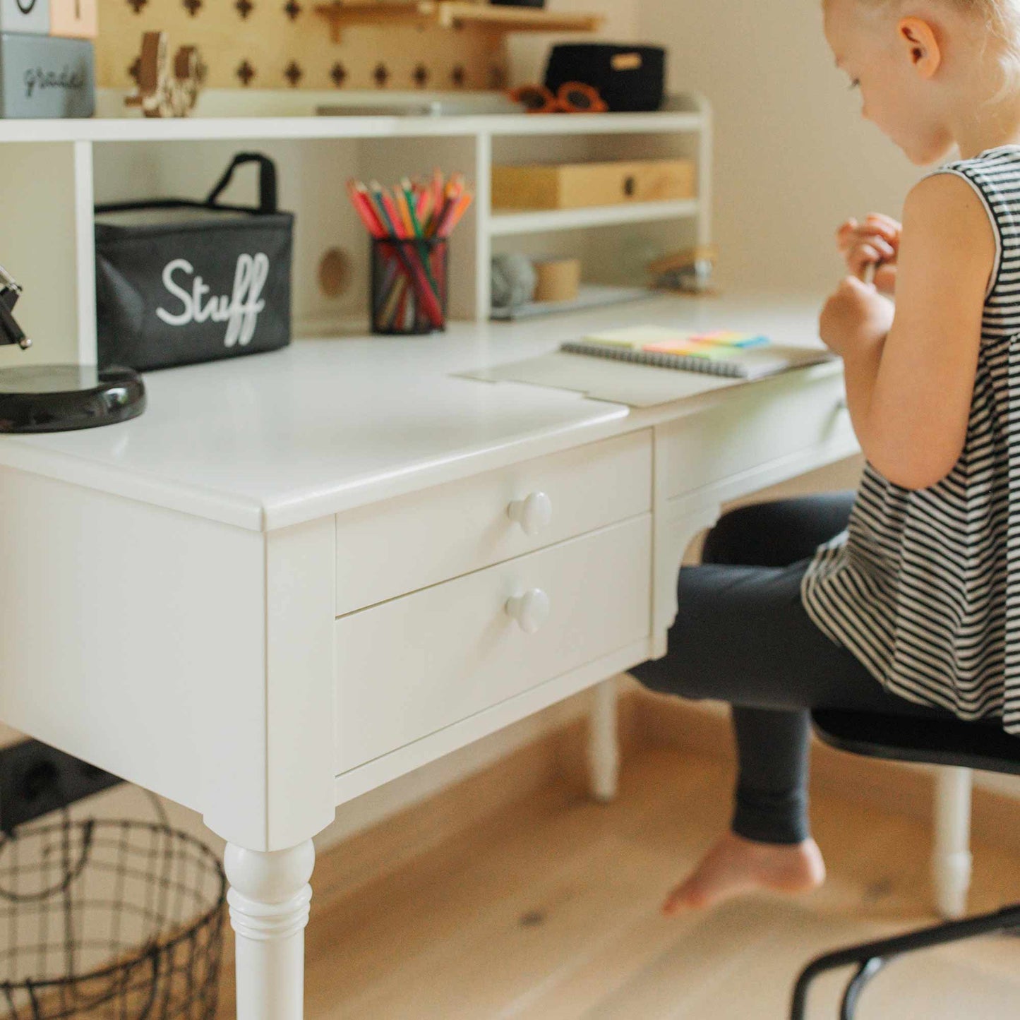 A child sits at the "Table with a Hutch, Pedestal Desk" with shelves and drawers, holding colored pencils and drawing in a notebook. This versatile desk features excellent cable management and ample storage space, perfect for keeping things tidy and organized.
