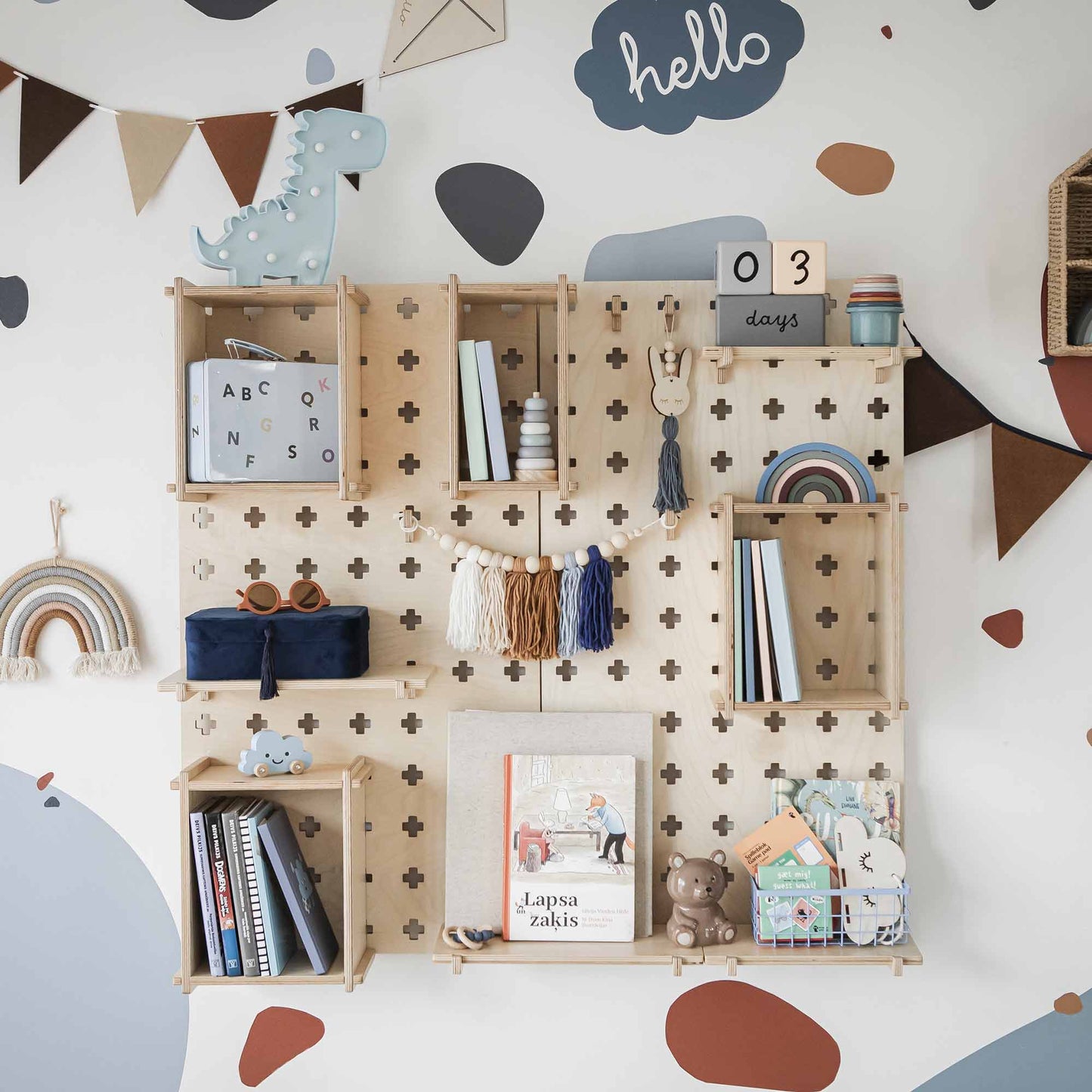 A well-organized nursery room wall is adorned with a Large Pegboard Shelf with Floating Shelves, holding books, toys, and decorations. A bunting banner and cloud-shaped signs enhance the playful decor, while customizable layouts provide flexible organizing solutions. A calendar display shows "03 days.