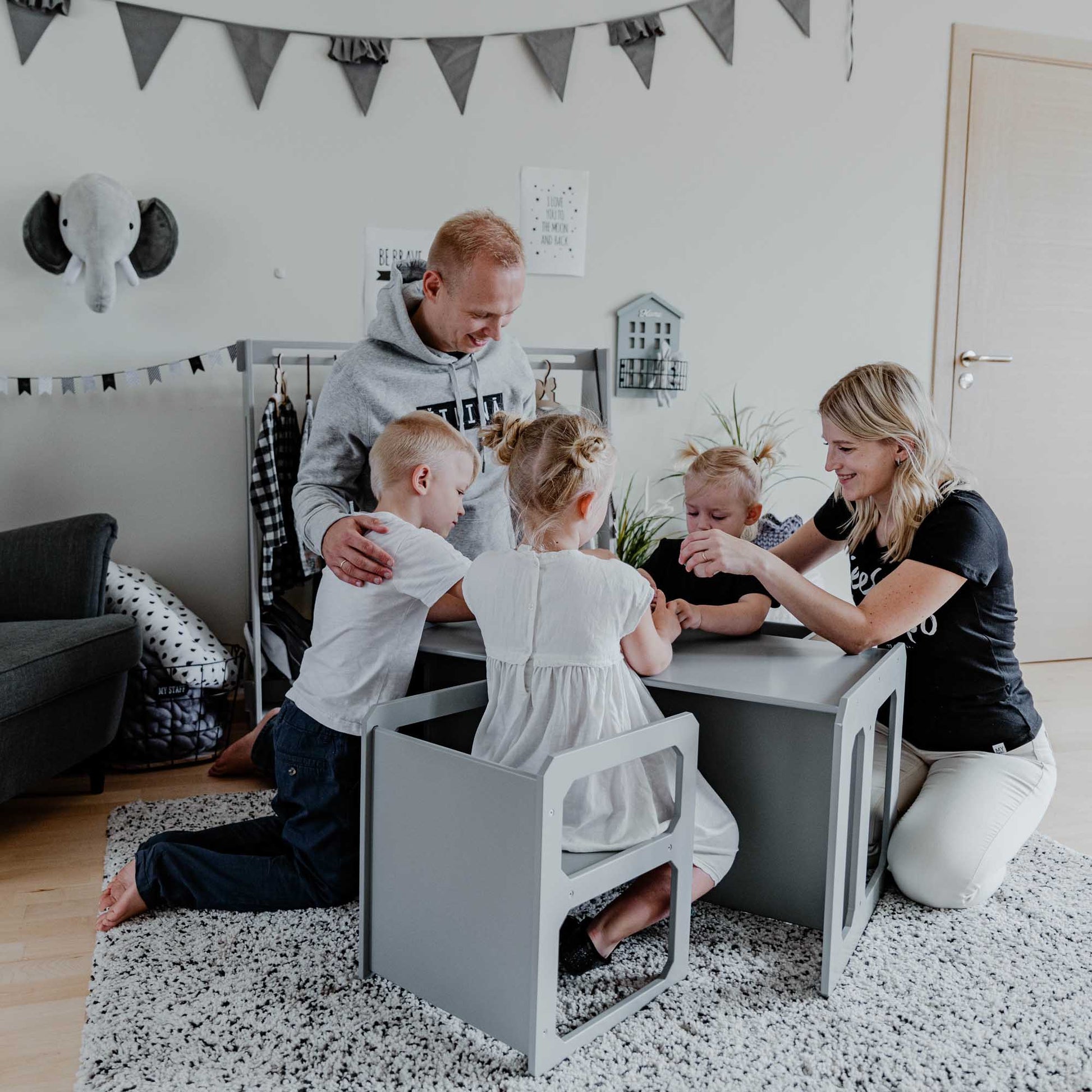 A family playing with their children at a Sweet Home From Wood Montessori weaning table and 2 chair set-equipped room.