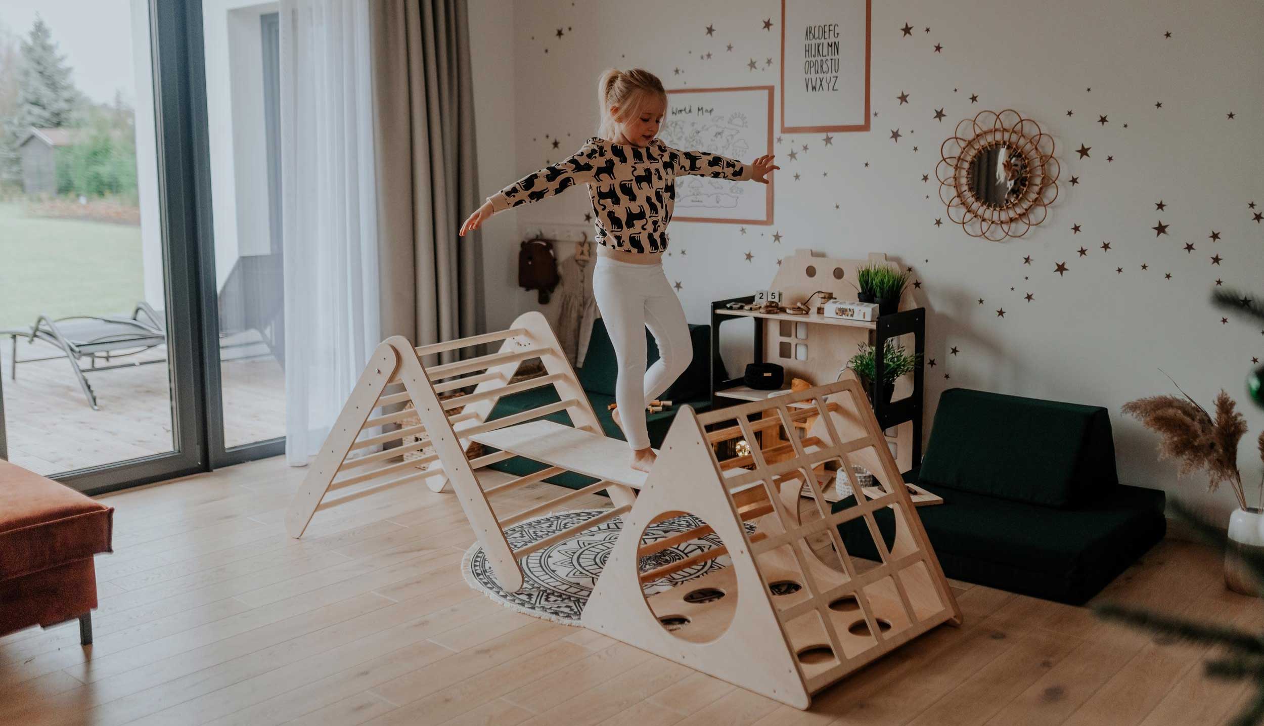 A girl is jumping on a wooden play set in a living room.
