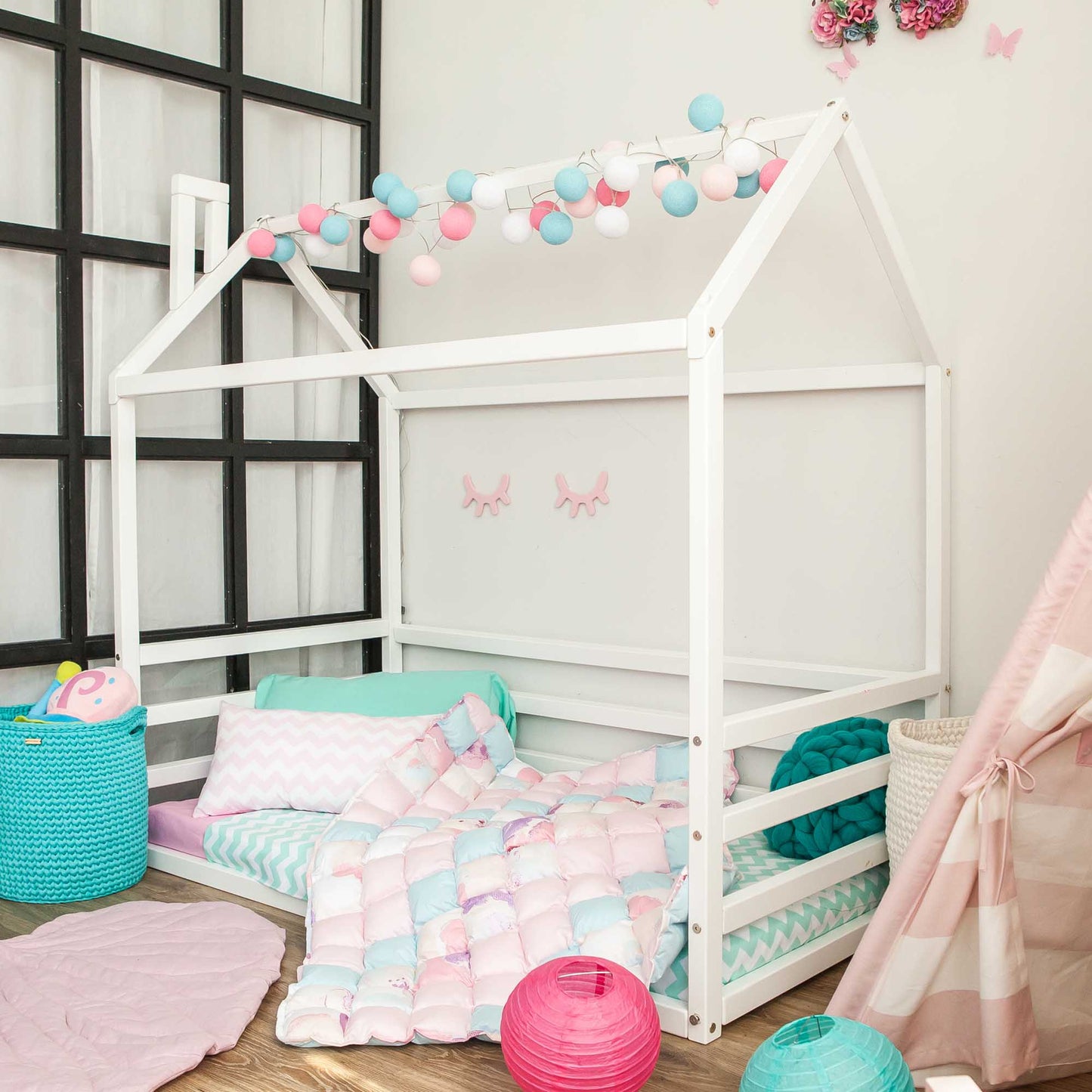 A girl's room with a white kids' house-frame bed with 3-sided horizontal rails and pink and blue decorations.
