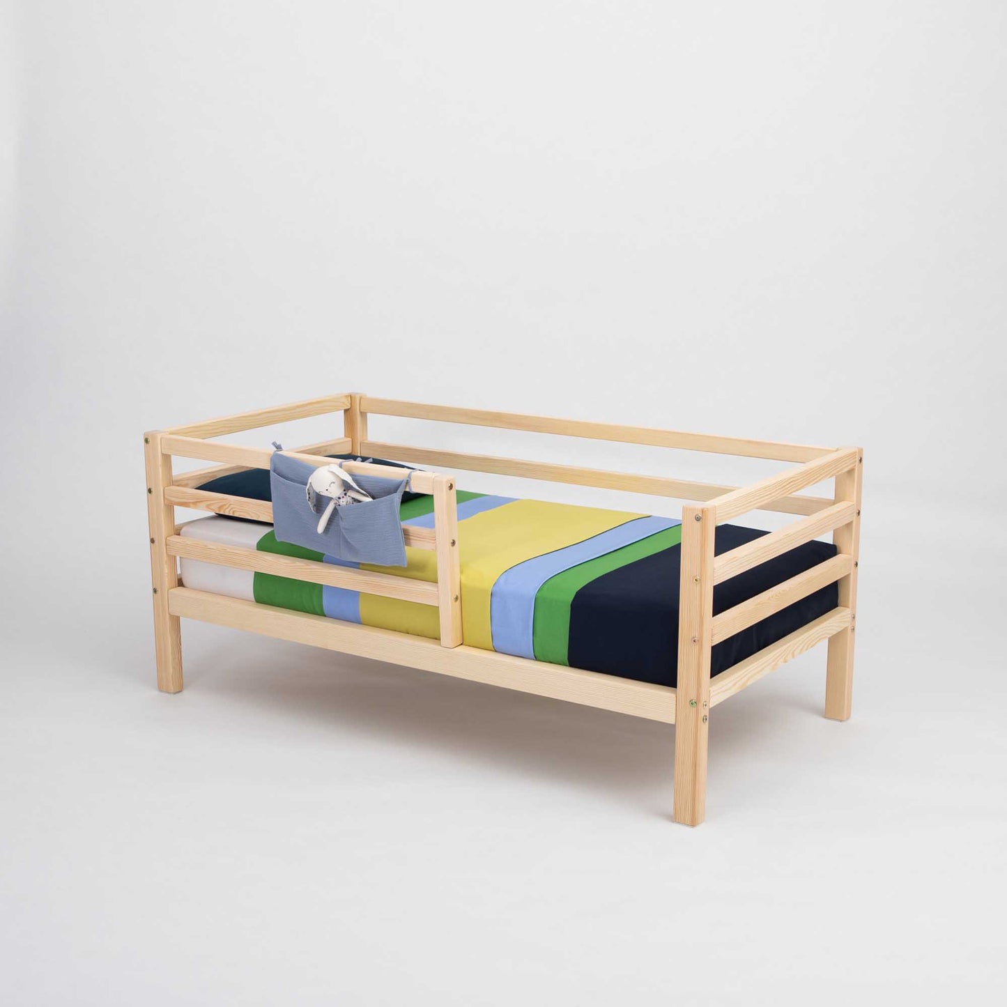 A 2-in-1 transformable kids' bed with a horizontal rail fence from Sweet Home From Wood, with a colorful striped blanket.