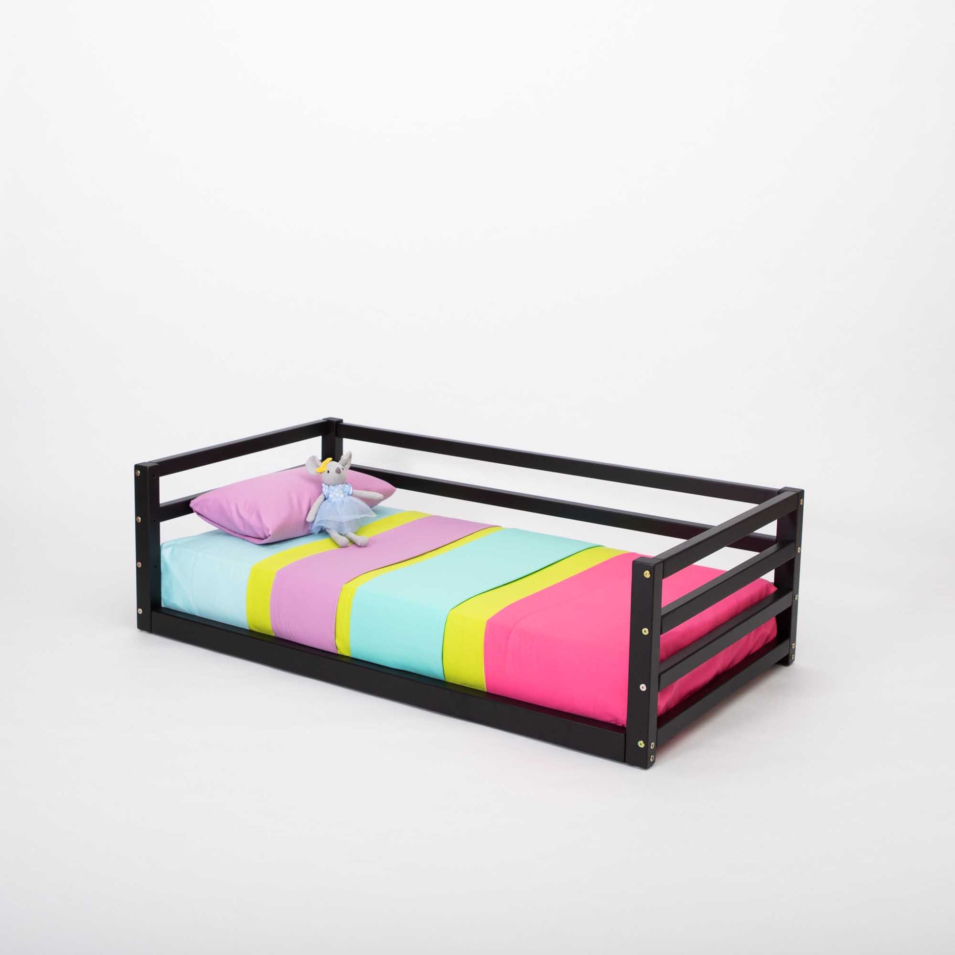 A Sweet Home From Wood children's floor level bed with colorful sheets, a black frame, and a 3-sided safety rail.