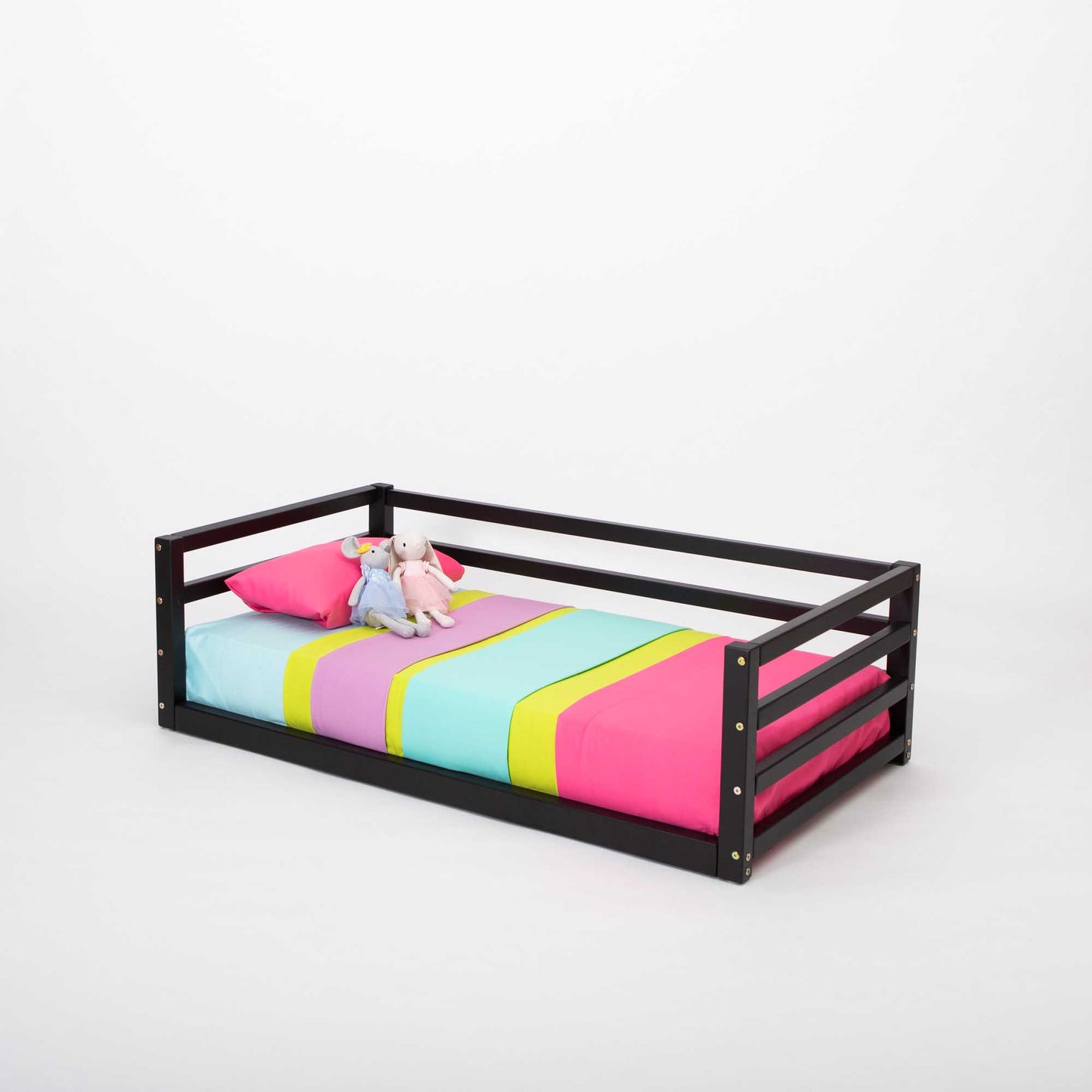 A Sweet Home From Wood children's floor level bed with colorful sheets and a black frame equipped with a 3-sided safety rail for transitional use.