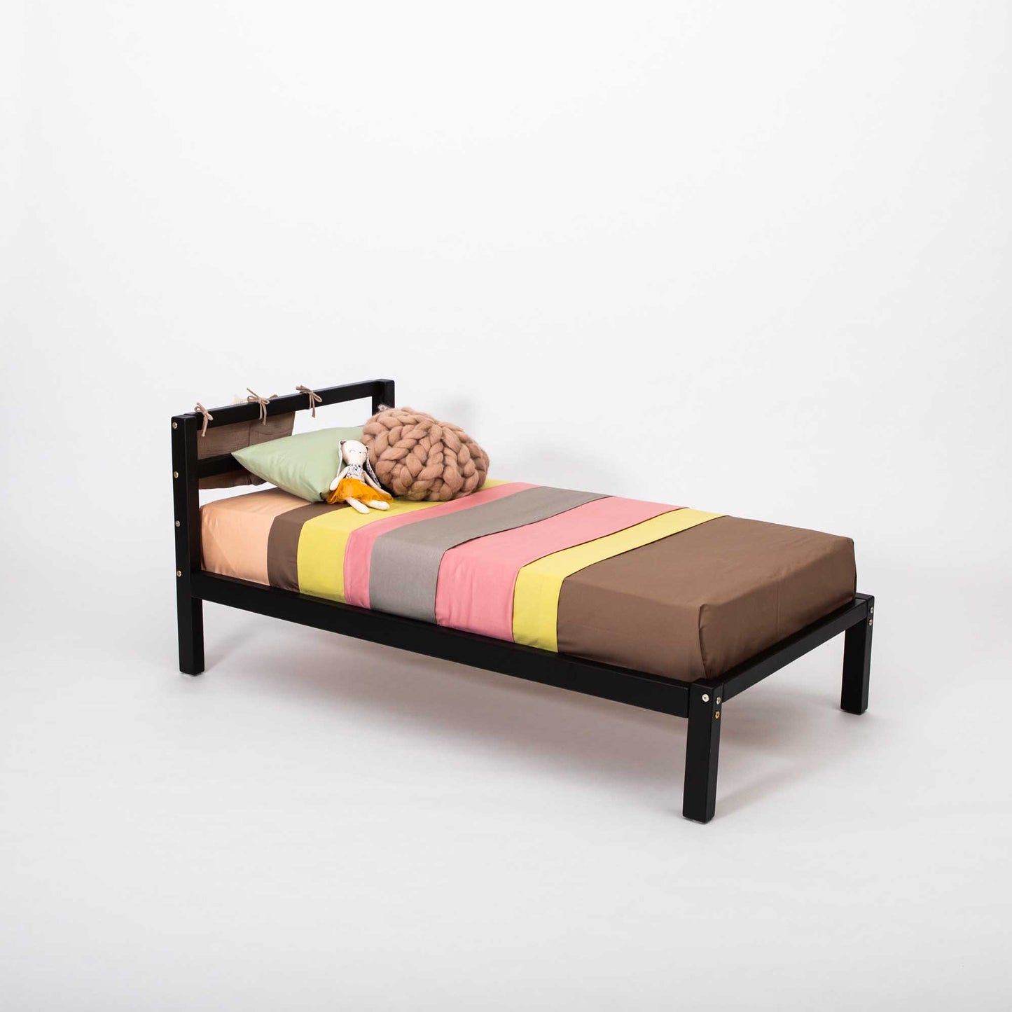A small black bed with a colorful striped blanket, featuring the Sweet Home From Wood 2-in-1 transformable kids' bed with a horizontal rail headboard, that can grow with the child.