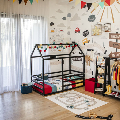 Children's room with car-themed decor featuring a Floor Level House Bed with a Horizontal Fence, toys, a clothes rack, and a play mat with a road design. Bright and colorful with wall decorations and a sliding glass door leading outside.